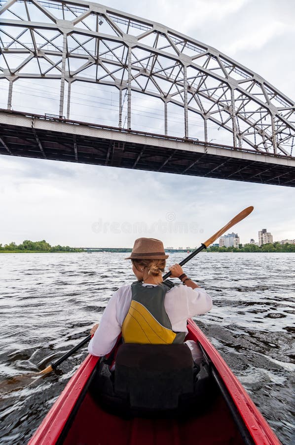 Oigenkännlig ung kvinna som kayaking på en flod Lycklig flicka som kanotar under metallbron på en sommardag
