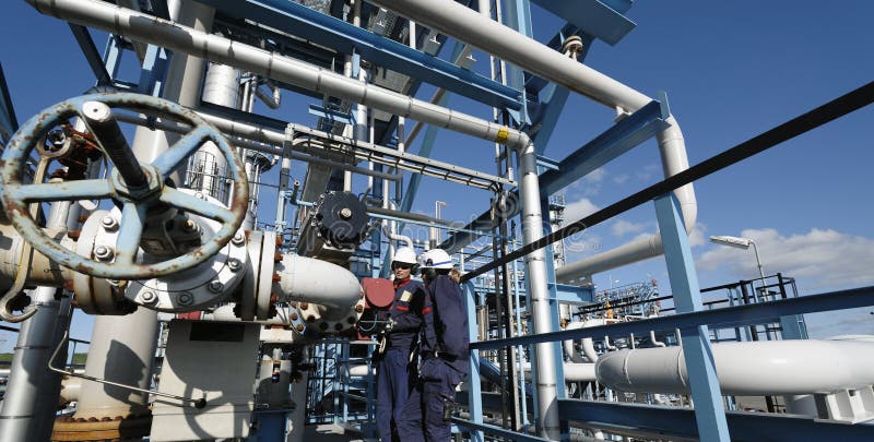 Two engineers, workers inside refinery, working on pipeline construction, one female worker. Two engineers, workers inside refinery, working on pipeline construction, one female worker.