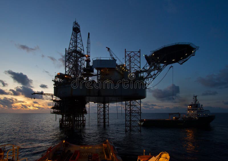 Oil rig platform with beautiful sky during sunset during cargo loading with an offshore vessel