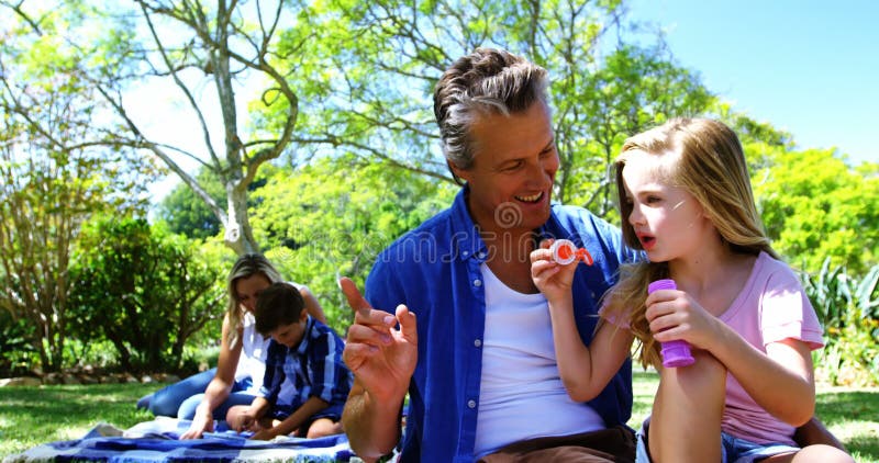 Ojca i córki dmuchanie gulgocze z bąbel różdżką przy pinkinem w parku 4k