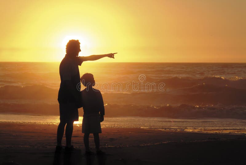 A father showing something to his son at sunset on a beach. A father showing something to his son at sunset on a beach