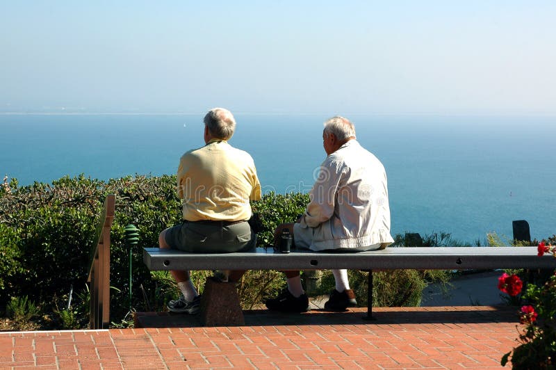 A son sits with his aging father on a bench overlooking the Pacific Ocean. A son sits with his aging father on a bench overlooking the Pacific Ocean.