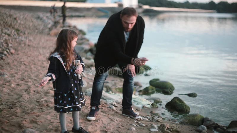 Ojciec i córka na brzeg, mała dziewczynka rzutu kamień w wodę Obsługuje przedstawienie dziewczyna jak sztuki kamienny omijać