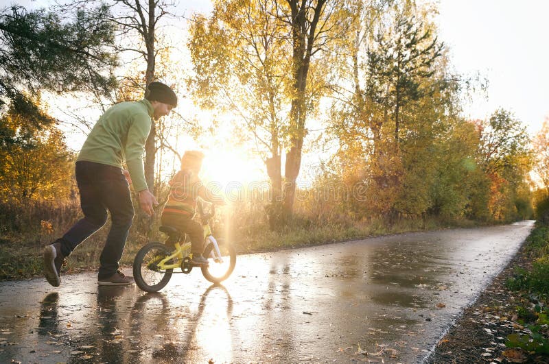 Ojciec uczy swojego małego dziecka jeździć na rowerze w jesiennym parku Szczęśliwe chwile rodzinne Razem z tatą i synem Candy