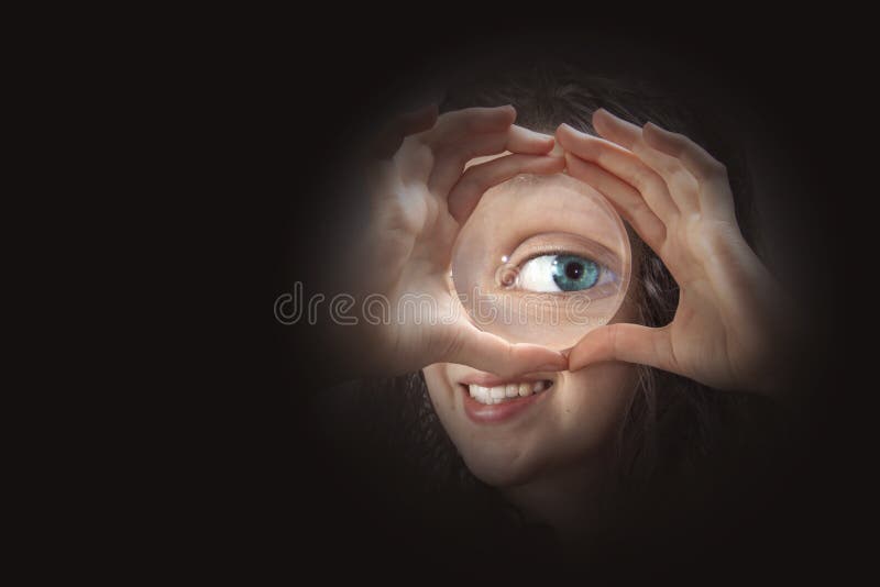 Female eye looking through magnifying glass close up, in a black background. Female eye looking through magnifying glass close up, in a black background