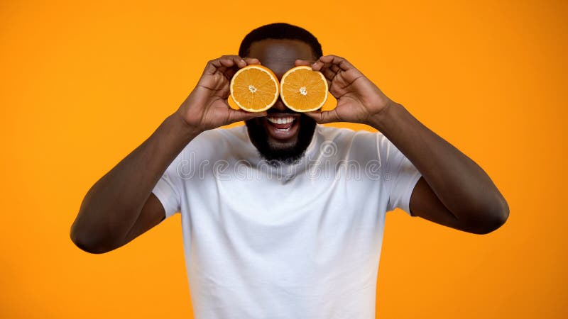 Ojos de cierre del hombre afroamericano alegre con la mitad de las naranjas, vitaminas para la salud