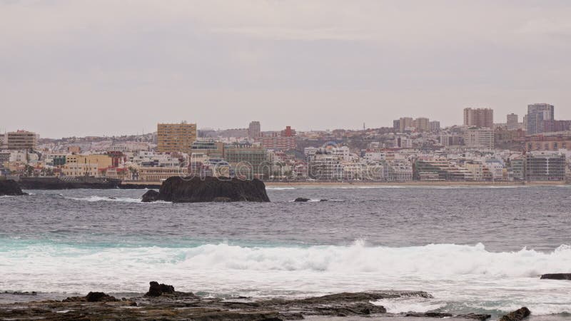 Olas estrellándose en la costa rocosa cerca del horizonte de la ciudad costera almacen de video