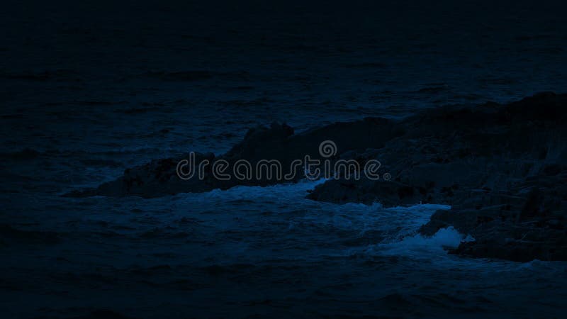 Olas oceánicas que se rompen en las rocas en la noche