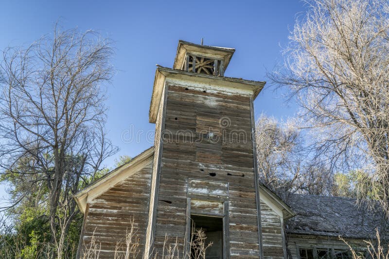 Old abandoned schoolhouse in rural Nebraska. Old abandoned schoolhouse with a bell tower in rural Nebraska overgrown by trees and weeds stock images Old abandoned schoolhouse in rural Nebraska. Old abandoned schoolhouse with a bell tower in rural Nebraska overgrown by trees and weeds stock images
