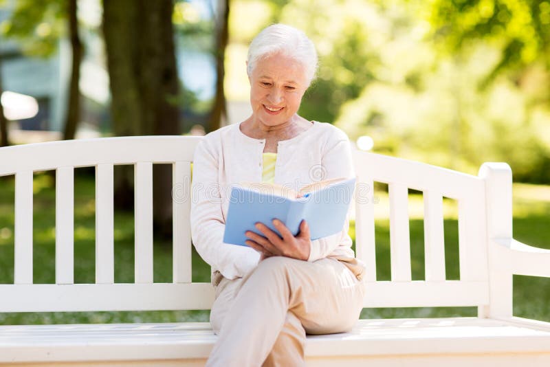 Old age, retirement and people concept - happy senior woman reading book sitting on bench at summer park. Old age, retirement and people concept - happy senior woman reading book sitting on bench at summer park