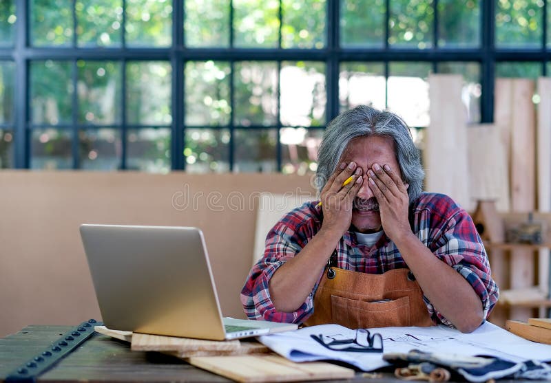 Old Asian craftsman act as feel bad or sad with something appear on laptop screen and sit in his workplace