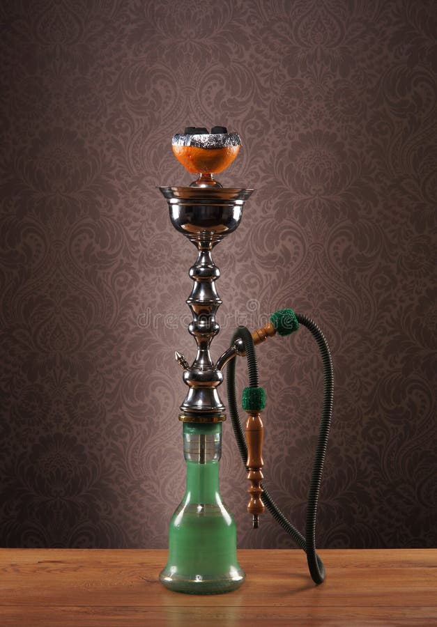 A beautiful old green ceramic hookah standing on a wooden desk. The image is taken in a studio on a vintage background. A beautiful old green ceramic hookah standing on a wooden desk. The image is taken in a studio on a vintage background.