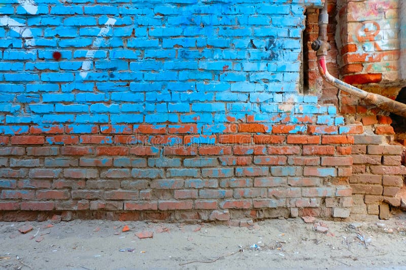 Old brick wall half painted in bright blue color and rusty water pipe, a lot of copyspace.