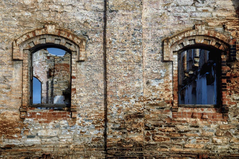 Old brick wall with windows of abandoned building. Grunge background of aged stone surface.