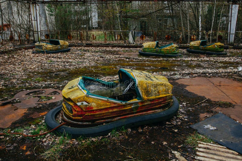 Old broken rusty metal radioactive yellow cars, children`s electric cars, abandoned among vegetation, the park of culture and rec
