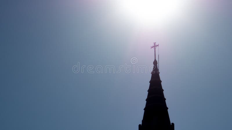 Church spire and steeple with sun shining above crucifix. Old catholic church steeple with sun shining brightly behind the crucifix atop the spire in silhouette