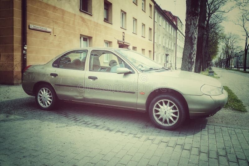 Big, old classic silver grey elegant Ford Mondeo first model sedan private car with four doors parked. Right side and front view. Old houses in the background. Retro photographic conversion. Faded colors. Big, old classic silver grey elegant Ford Mondeo first model sedan private car with four doors parked. Right side and front view. Old houses in the background. Retro photographic conversion. Faded colors.