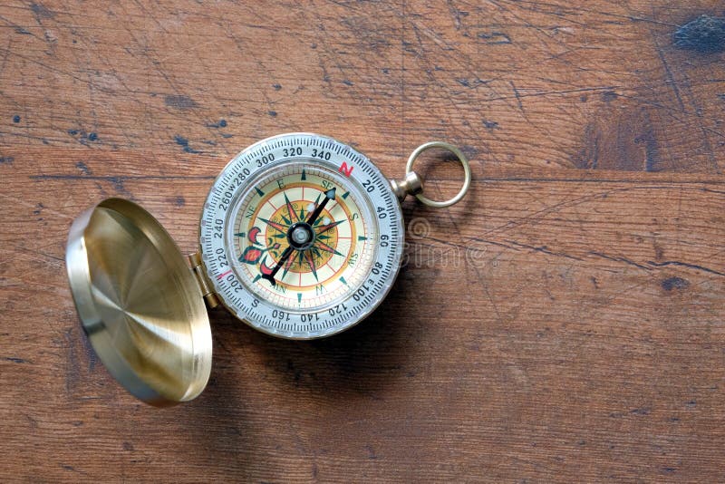 Old compass in brass case on vintage wooden background top view closeup. Old compass in opened brass case on vintage brown wooden background shown to Nord stock images Old compass in brass case on vintage wooden background top view closeup. Old compass in opened brass case on vintage brown wooden background shown to Nord stock images