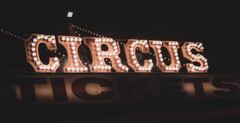 Old dimly lit circus sign with light bulbs in the dark over a ticket stand. Typical view of an entrance to a circus. Concept of