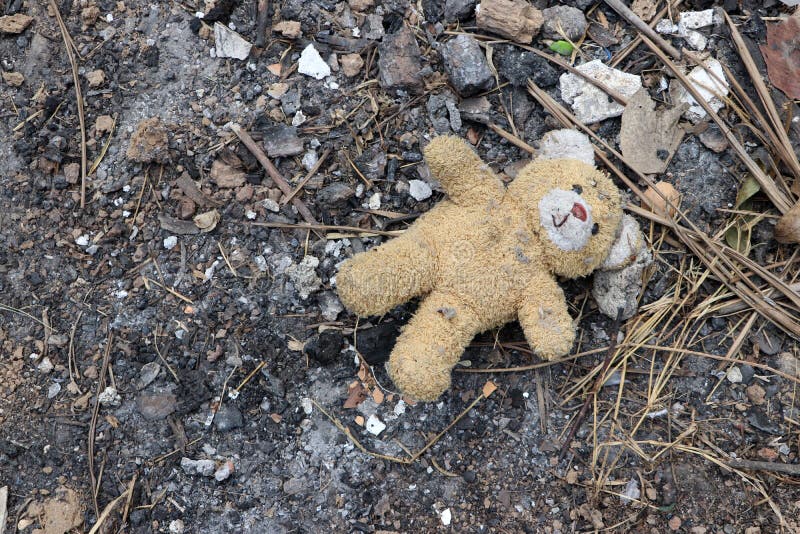 Old dirty teddy bear neglected on the ground soil. End of childhood stock image
