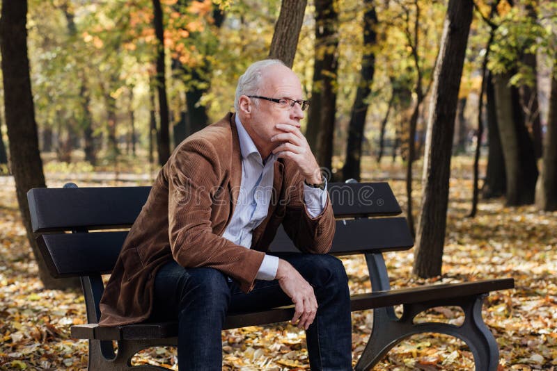 Old elegant man sitting on bench outside.