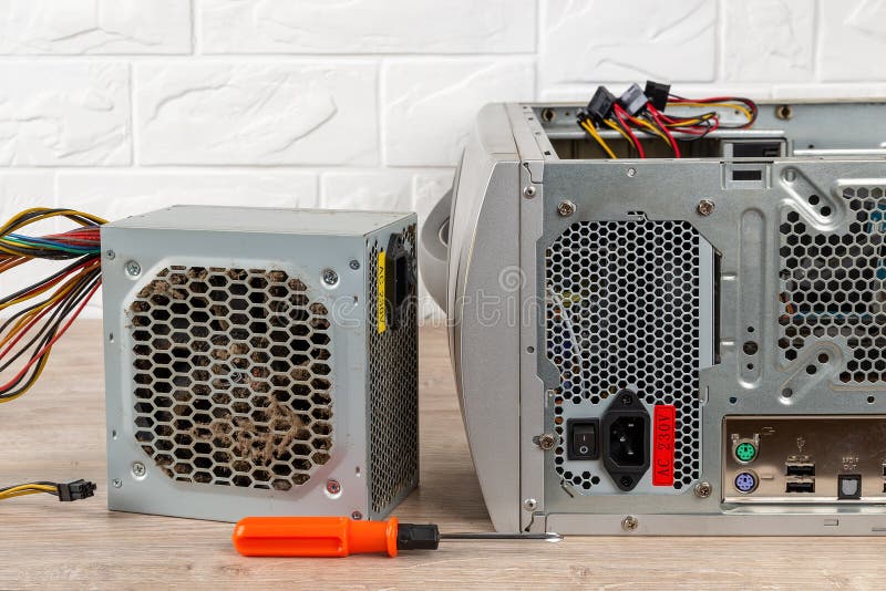 Old faulty power supply unit and a screwdriver near tower case with installed new one on a desk. Personal computer PSU replacement stock photography