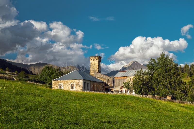 Old georgian house with ancient svan defensive tower on a green meadow with blue sky and clouds on a background