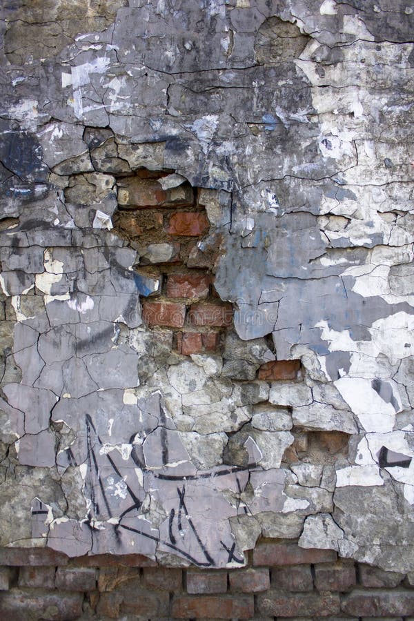 Old gray heavily damaged concrete wall with deep relief and protruding red bricks, cracks and various stains of paint and dirt. stock photos Old gray heavily damaged concrete wall with deep relief and protruding red bricks, cracks and various stains of paint and dirt. stock photos