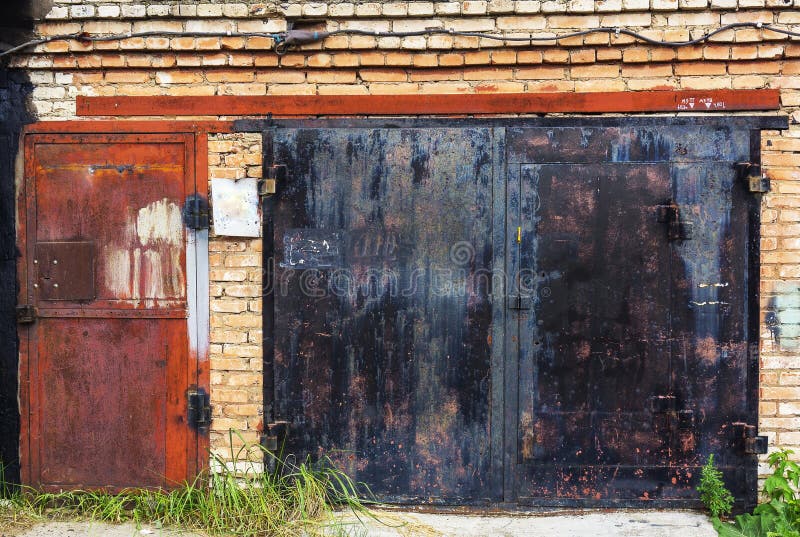 Old grunge metal doors of garage made of bricks with plants grew around on spring summer season vintage retro style