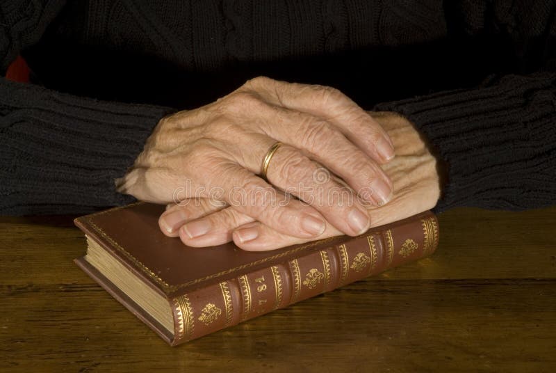 Old hands with weddingring resting at closed antique bible. Old hands with weddingring resting at closed antique bible