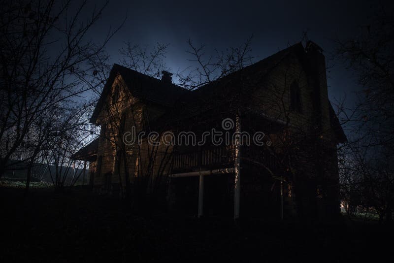 Old house with a Ghost in the forest at night or Abandoned Haunted Horror House in fog. Old mystic building in dead tree forest.