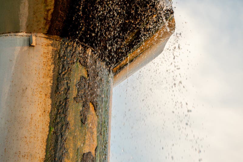 An old leaky water tower. Water flows from a large iron barrel. Broken metal construction