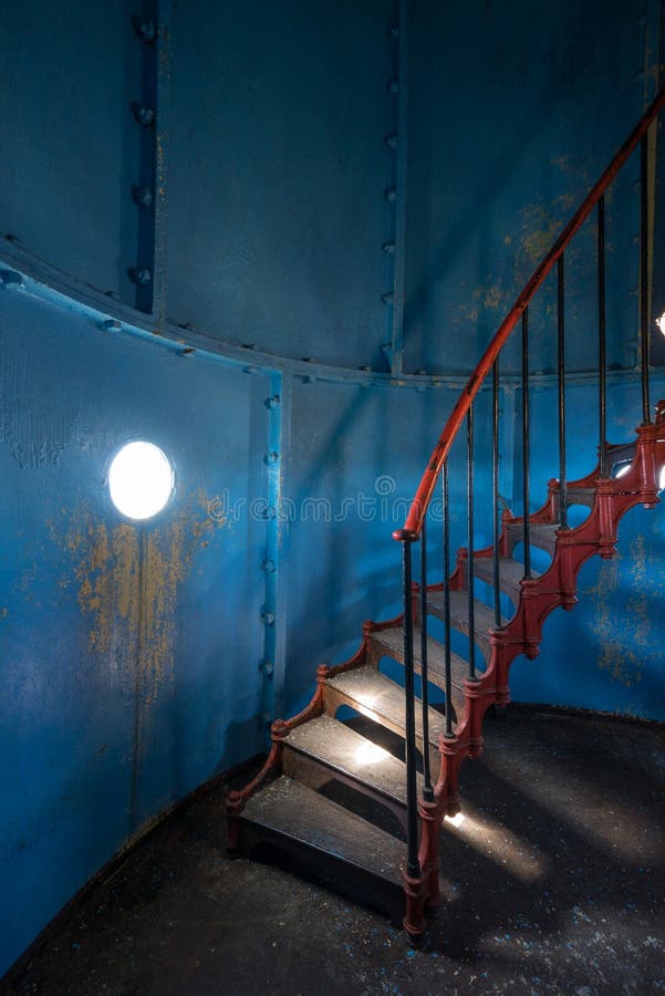 Old lighthouse on the inside. Red iron spiral stairs, round window and blue wall