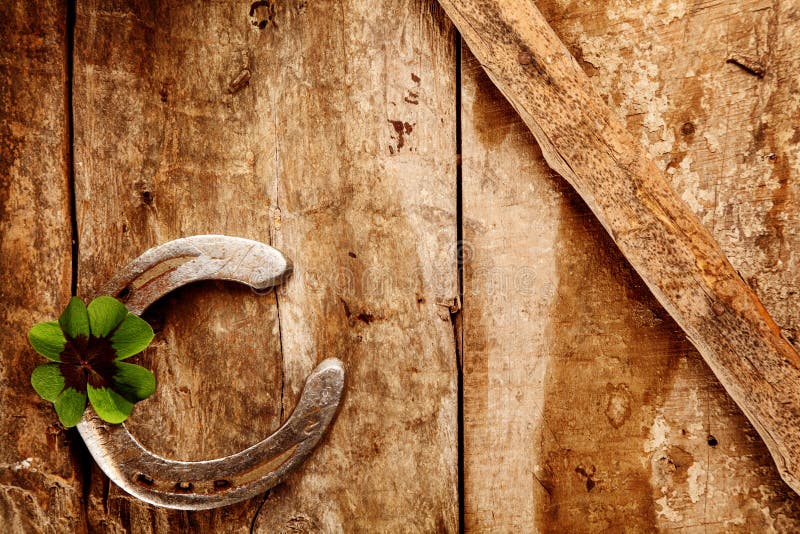 Old lucky horseshoe background with the horseshoe arranged in the corner with a green Irish shamrock for double luck on a rustic wooden background with copyspace,