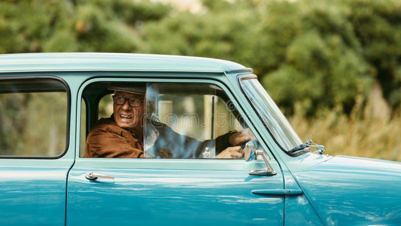 Senior man driving a classic car. Old man looks out of the window of his car before making a turn on road. Senior man driving a classic car. Old man looks out of the window of his car before making a turn on road.