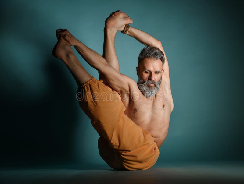 Old man with grey beard doing yoga, pilates, fitness training, stretching exercise, asana or balance workout on floor