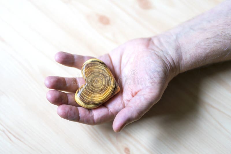 Old man holding a wooden heart in his hands, a gift for Valentine`s Day, focus on hands and a heart. Horizontal frame, closeup