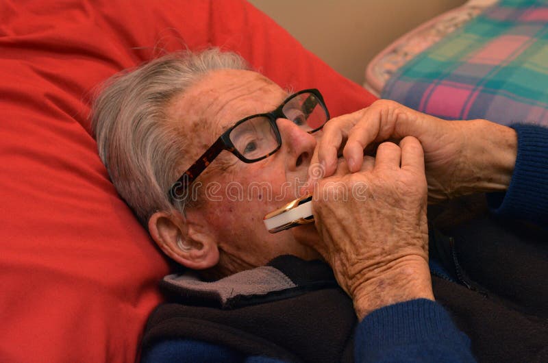 Old man play harmonica in bed. Concept photo of old age, lonely, alone, retirement, music, sad.
