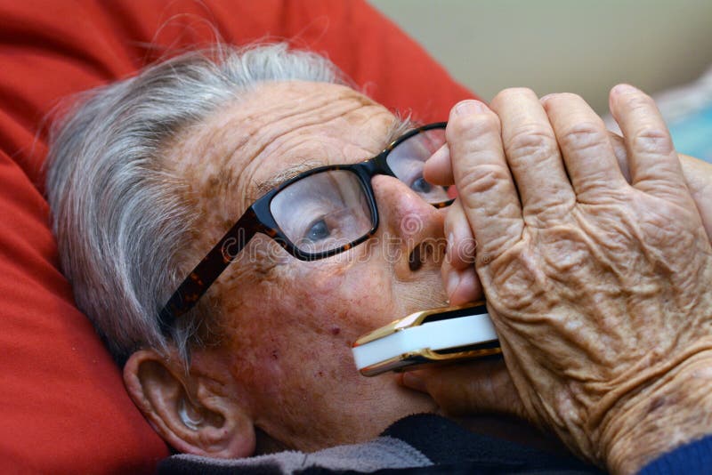 Old man play harmonica in bed. Concept photo of old age, lonely, alone, retirement, music, sad.