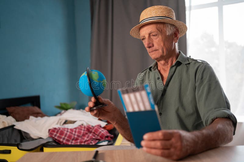 Old man preparing on a trip, choosing a country on globe, sitting at home, preparing for vacation after retirement. royalty free stock photography