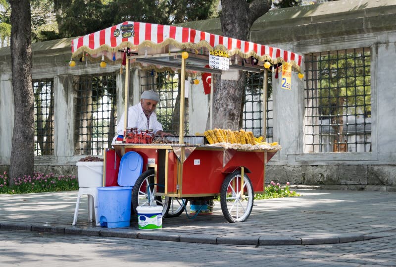 Istanbul, Turkey - April 16, 2017: Old man selling chestnut and corn on traditional Turkish fast food cart in Sultan Ahmed Square. Istanbul, Turkey - April 16, 2017: Old man selling chestnut and corn on traditional Turkish fast food cart in Sultan Ahmed Square