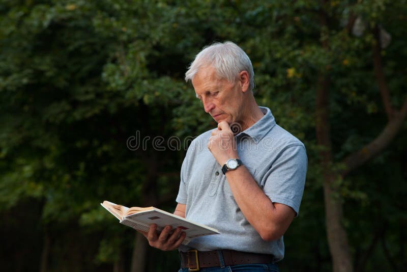 Viejo hombre de pie a lectura un libro en el parque.