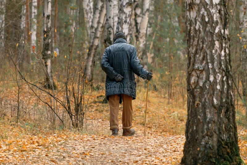 An old man walks holding his lower back with a cane in his hand