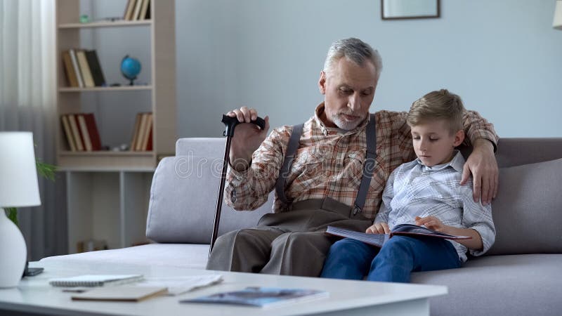 Old man watching photo album with grandson, recalling stories from happy youth