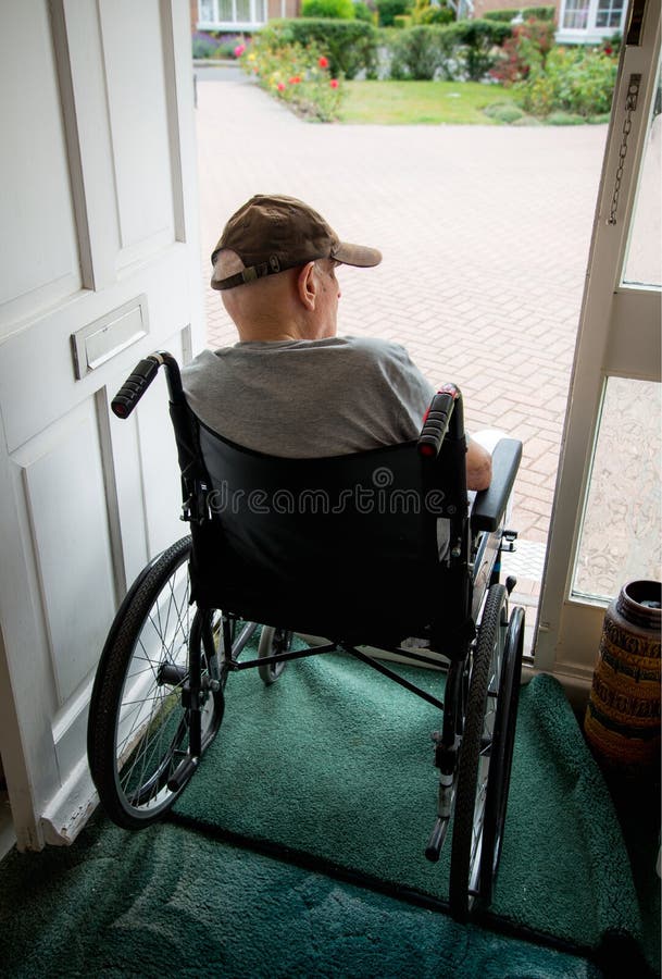 Old man in wheelchair looking out from the open doorway of his house.Hampshire,United Kingdom