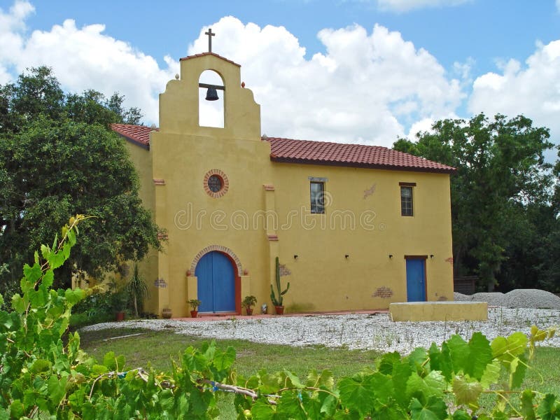 A colorful, Mexican adobe-style church against a blue sky with grape vines in the foreground. A colorful, Mexican adobe-style church against a blue sky with grape vines in the foreground.