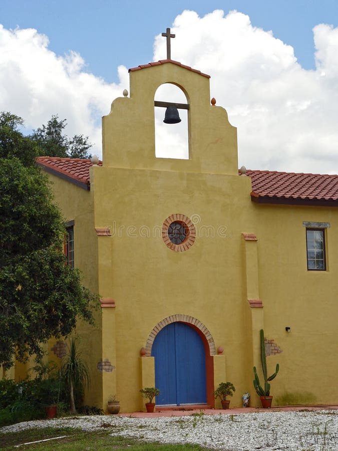 A colorful, Mexican adobe-style mission church with a bell tower against a bright blue sky. A colorful, Mexican adobe-style mission church with a bell tower against a bright blue sky.