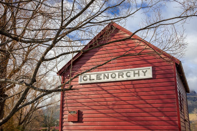 Old red boatshed, Glenorchy, New Zealand. Colourful scene, wooden shed, bare trees and blue, cloudy sky background