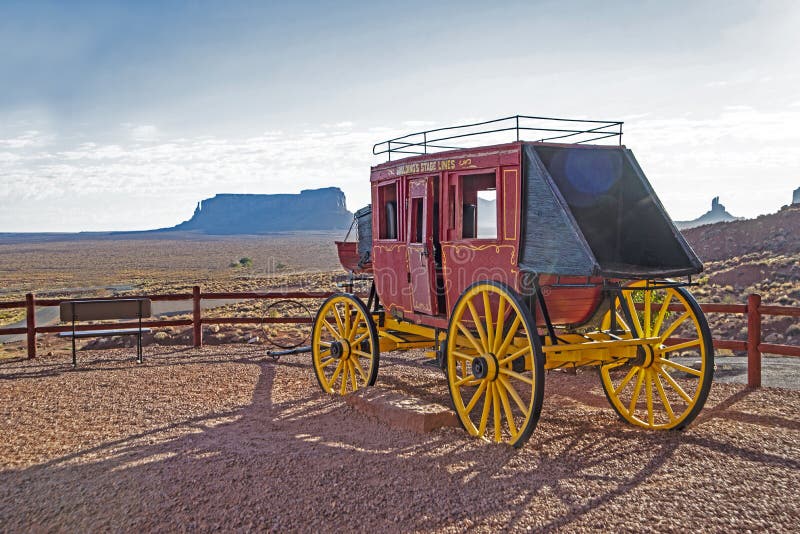 An old red stagecoach is on display beneath red rock cliffs.