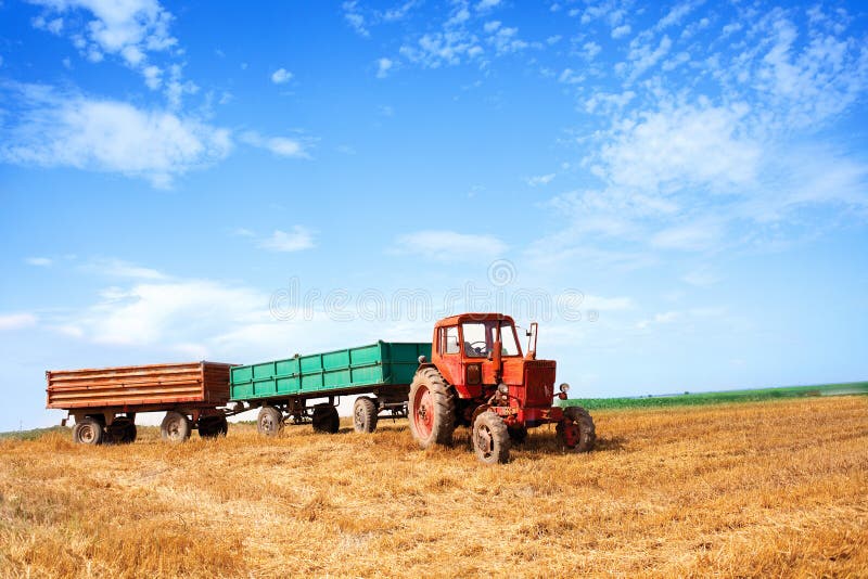 Old red tractor and trailers during wheat harvest on cloudy summer day stock photos